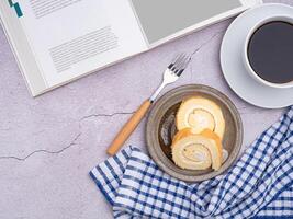 Top view of a book with roll cakes on a plate, a white coffee cup, and a cloth placed on a gray stone background. Space for text. Concept of relaxation photo