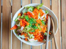 Japanese salad in a bowl with bamboo cutlery placed on a wooden table. Close-up photo. Top view with copy space for text. Concept of healthy foods and vegetables photo