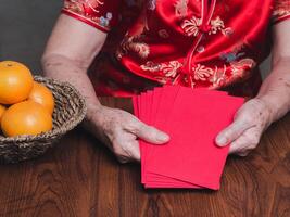 Hands of a senior woman holding red envelopes or Angpao wearing a traditional cheongsam qipao dress while sitting in the studio. Chinese New Year photo