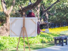 Back view of a wooden easel with white canvas in the park. Drawing easel. Copy space for your text. Concept of art and drawing photo