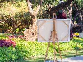 Back view of a wooden easel with white canvas in the park. Drawing easel. Copy space for your text. Concept of art and drawing photo