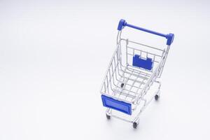 Mini shopping cart with a blue handle on white background. High angle of view. Space for text. Concept of shopping and e-commerce photo