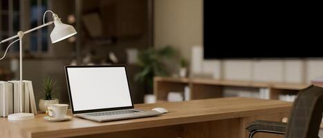 A laptop computer with a white-screen mockup is on a wooden desk in a cozy, minimal home office. photo