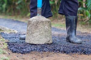 Man holding a cement rod for hammering to adjust the asphalt surface for the walkway. Close-up photo. Constructed from asphalt. Space for text photo
