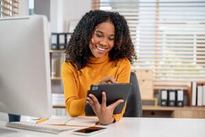 An attractive, positive Black businesswoman using her digital tablet at her desk in the office. photo