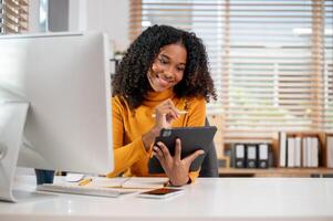 An attractive, positive Black businesswoman using her digital tablet at her desk in the office. photo