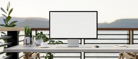 A computer desk on a balcony with a mountain view, a computer with a white-screen mockup. photo