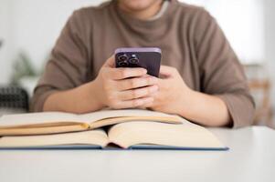 A cropped image of a female college student using her smartphone while reading a book. photo