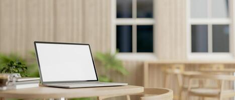 A laptop computer with a white-screen mockup on a table in a comfortable minimalist cafe. photo
