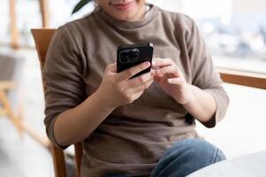 A cropped image of an Asian woman in casual clothes is using her smartphone while chilling in a cafe photo