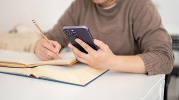 A cropped image of a student using her smartphone while doing homework in a cafe or a library. photo