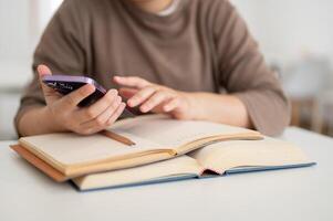 A cropped image of a female college student using her smartphone while reading a book. photo