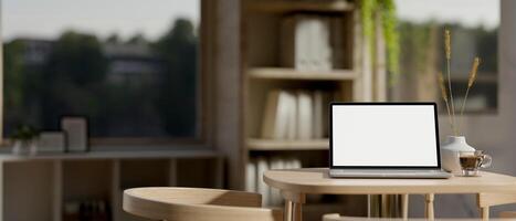 A close-up image of a laptop computer with a white-screen mockup on a wooden table in a cozy room. photo