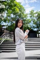 A beautiful Asian businesswoman with a file folder is smiling at the camera while standing outdoors. photo