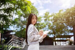 atractivo asiático mujer de negocios con un archivo carpeta y un café taza, en pie en el escalera al aire libre. foto