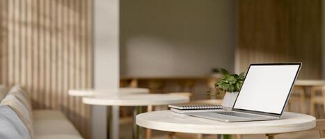 A laptop computer with a white-screen mockup on a table in a modern, comfortable coffee shop. photo