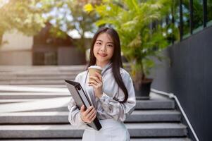 atractivo asiático mujer de negocios con un archivo carpeta y un café taza, en pie en el escalera al aire libre. foto