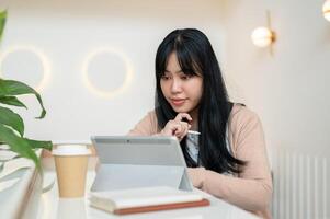 un hermoso, pensativo joven asiático mujer enfoque en leyendo alguna cosa en su digital tableta. foto
