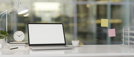 Modern office features a laptop computer with a white-screen mockup and accessories on a white desk. photo