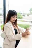 A businesswoman in a white suit is relaxing in a cafe, having a coffee and using her smartphone. photo