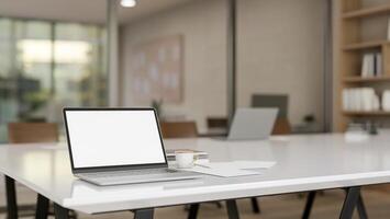 A laptop computer with a white-screen mockup on a meeting table in a meeting room. photo