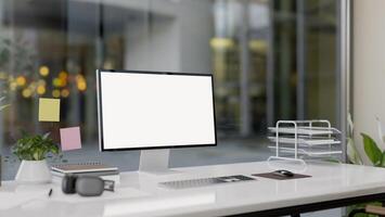 A modern office features a computer with a white-screen mockup and office supplies on a white desk. photo