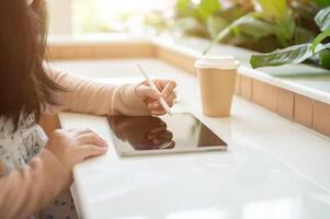 un recortado imagen de un positivo asiático mujer utilizando su tableta a un mesa en un minimalista café tienda. foto