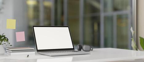 A modern office features a laptop computer with a white-screen mockup on a white desk. photo