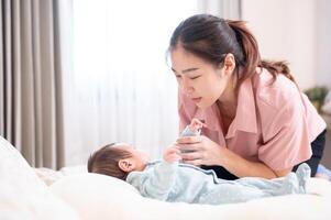 un cuidando joven asiático mamá poniendo su infantil bebé a dormir en el dormitorio. foto