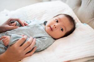 un adorable asiático recién nacido bebé hijo en azul pijama es en su cama, hablando y jugando con su mamá. foto