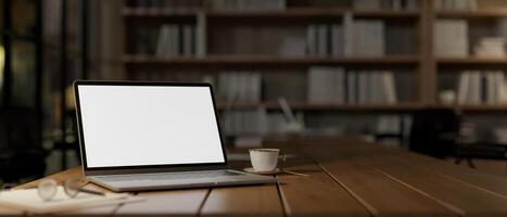A close-up image of a laptop mockup on a wooden table in a cozy reading library room or home office. photo