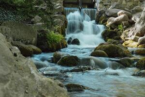 Waterfall cascade in Olivia public park Gdansk Poland. River waterfall falls from cliff and trees. Tourist attraction with small waterfall and clear water Long exposure Unity with nature photo