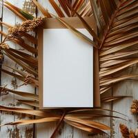Top view of a blank white sheet of paper on a rustic wooden surface, surrounded by dried palm leaves and wheat. photo