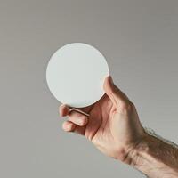 Close-up of a hand holding a white blank circular object against a neutral background. Perfect for mockups, design, and concept art. photo