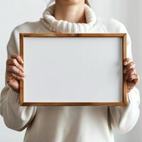 Person in white sweater holding blank wooden frame on white background, ready for customization or message insertion. photo