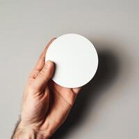 Close-up of a hand holding a blank white circular card against a neutral background. Ideal for mockups, designs, and message presentations. photo