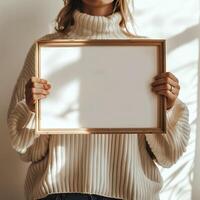 Person in a cozy sweater holding an empty wooden frame against a white background, ready for customization or artwork display. photo