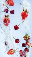 Fresh strawberries and cherries submerged in water, with bubbles rising against a light blue background. Refreshing and vibrant summer fruits. photo