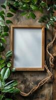 Vertical wooden picture frame surrounded by lush green foliage and rustic rope on a wooden textured background. photo
