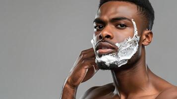 A man with a confident look applying shaving cream to his face The gray background highlights his wellgroomed appearance and skincare routine photo