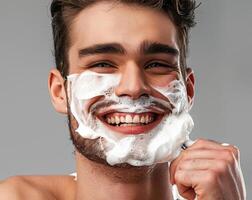 A smiling man applying shaving cream to his face, with a gray background that enhances his clear and smooth skin Perfect for advertisements promoting mens skincare and grooming routines photo