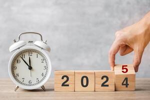 Happy New Year with vintage alarm clock and hand flipping 2024 change to 2025 block. Christmas, New Start, Resolution, countdown, Goals, Plan, Action and Motivation Concept photo
