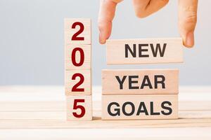 hand holding wooden block with text 2025 NEW YEAR NEW GOALS on table background. Resolution, strategy, solution, business and holiday concepts photo