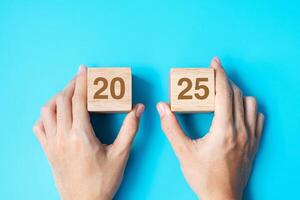 hand holding wooden cube block with 2025 text on blue background. Resolution, plan, review, goal, start and New Year holiday concepts photo