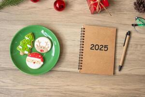 2025 notebook, black, Christmas cookies and pen on wood table, Top view and copy space. Xmas, Happy New Year, Goals, Resolution, To do list, Strategy and Plan concept photo