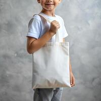 Tote bag mockup. Smiling boy carrying reusable white cotton eco organic fabric canvas blank totebag on grey background photo