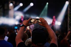 Person standing in front of stage, recording live music concert on smartphone photo