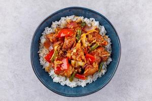 Rice with pork and vegetables in a sweet and sour sauce on a grey background, for a restaurant menu or food delivery photo
