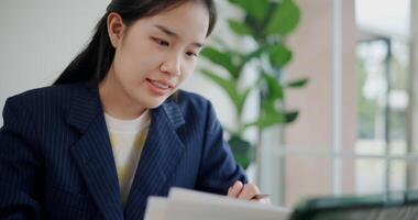 Portrait of Asian businesswoman in suit use digital tablet for work and analyze documents in small coffee shop. Work from anywhere, Remote working photo
