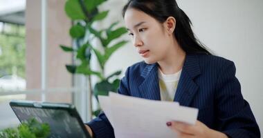 Portrait of Asian businesswoman in suit use digital tablet for work and analyze documents in small coffee shop. Work from anywhere, Remote working photo